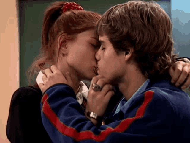 a boy and a girl kissing in front of a green board