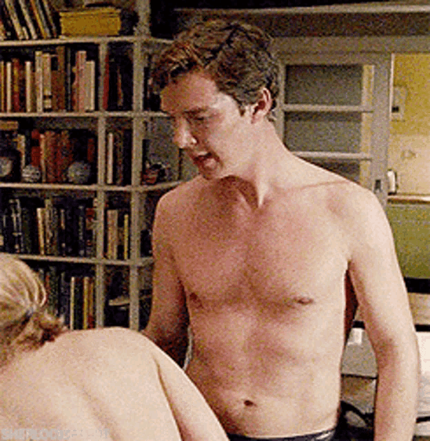 a shirtless man is standing next to a woman in front of a bookshelf