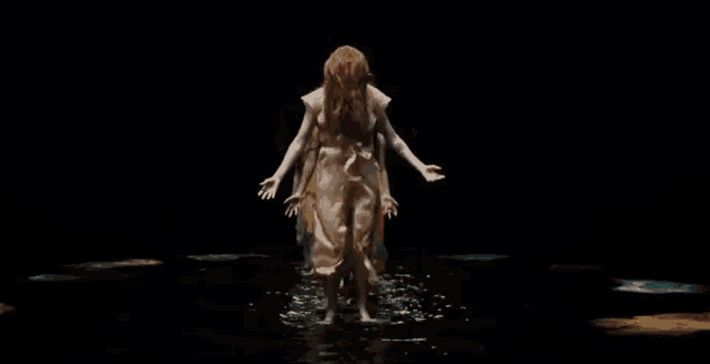 a group of women are standing in the water with their arms outstretched in a dark room