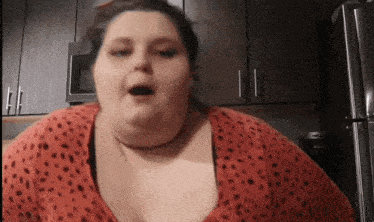 a woman in a red shirt with black polka dots is standing in front of a refrigerator