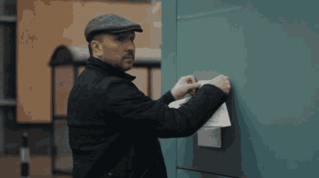 a man wearing a hat is putting a piece of paper on a green wall