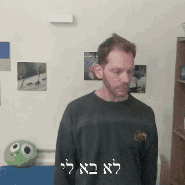 a man stands in front of a wall with pictures on it and a green stuffed animal