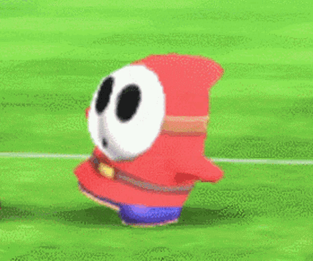 a shy guy from super mario bros is jumping in the air on a green field .