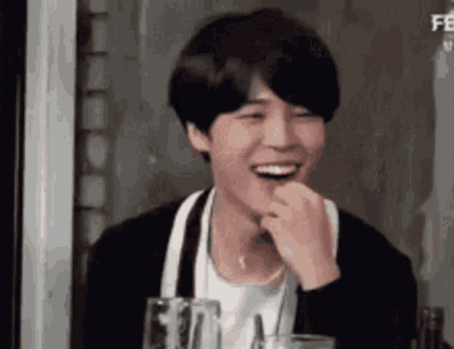 a man is laughing while sitting at a table with a glass of beer in front of him .