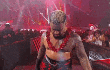 a wrestler wearing a red lei is walking through a crowd of people .