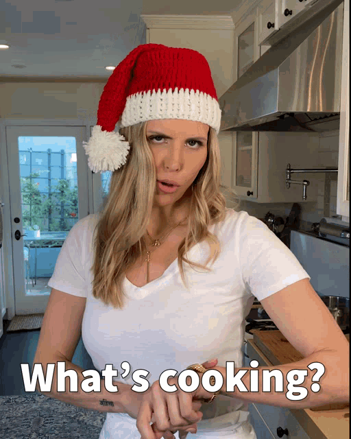 a woman wearing a santa hat is asking what 's cooking in a kitchen