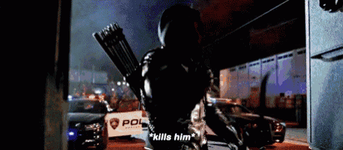a man in a black suit is holding an arrow and says `` kills him '' while walking down a street .