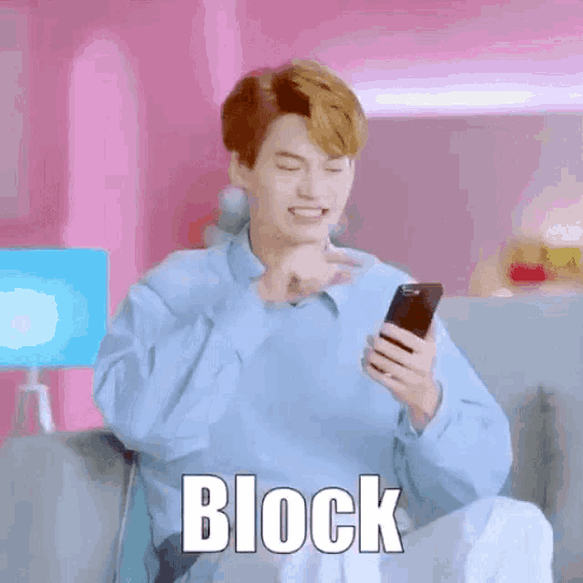 a young man is sitting on a couch looking at a cell phone and making a funny face .