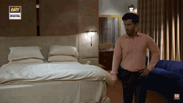 a man in a pink shirt stands in front of a bed in a bedroom with ary digital written on the wall