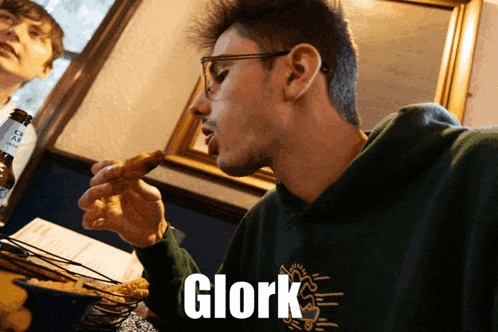 a man in a green hoodie is eating a chicken wing with the word glork on the bottom