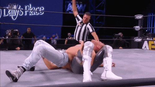 a wrestler is laying on the ground while a referee holds up his hand