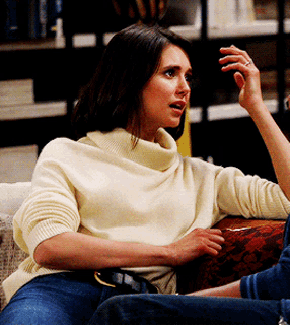 a woman in a white sweater sits on a couch talking