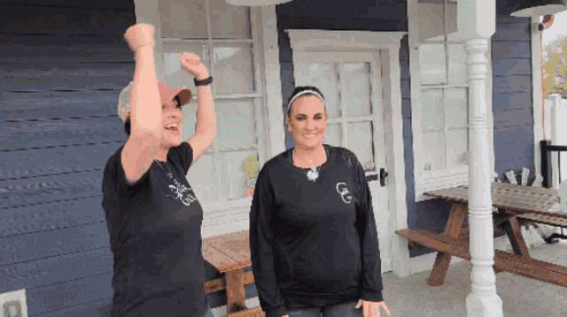 two women standing in front of a blue building with one wearing a shirt that says ' cc ' on it