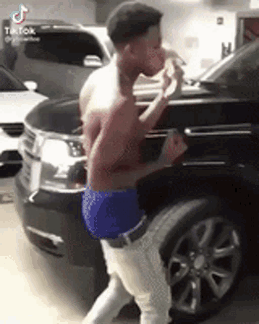a shirtless man in blue shorts is standing in front of a black car .