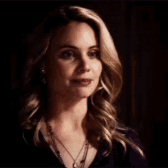 a close up of a woman 's face in a dark room wearing a necklace .