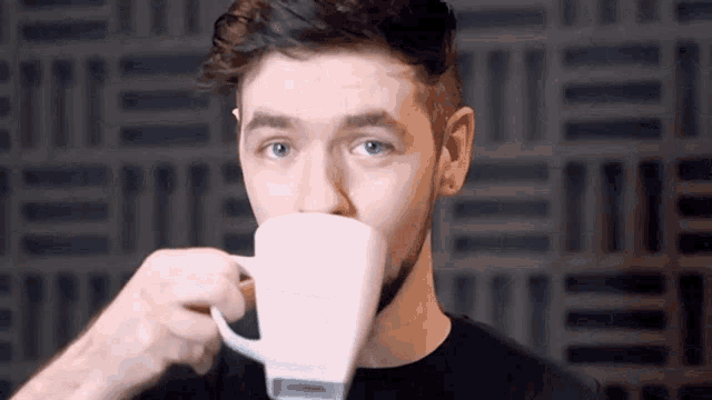 a young man with a beard is drinking from a white mug .