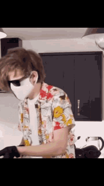 a man wearing a face mask and sunglasses is standing in a kitchen .