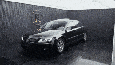 a black car is parked in front of a wall with a r on it