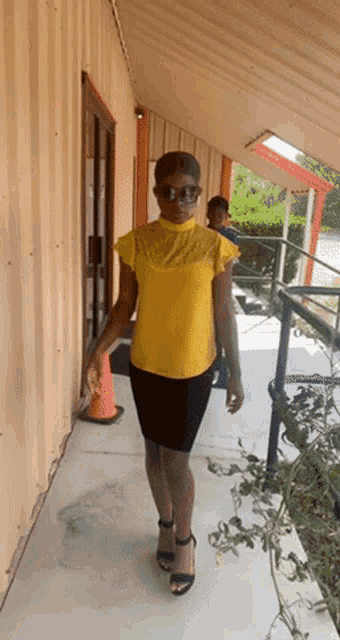 a woman wearing a yellow top and black skirt is walking down a sidewalk