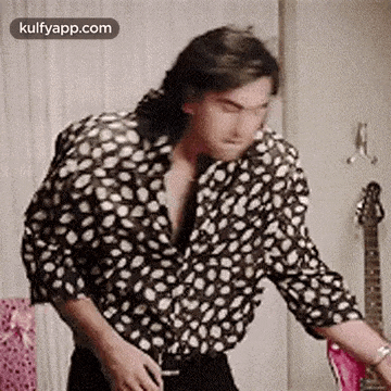 a man in a black and white polka dot shirt is standing in front of a guitar .