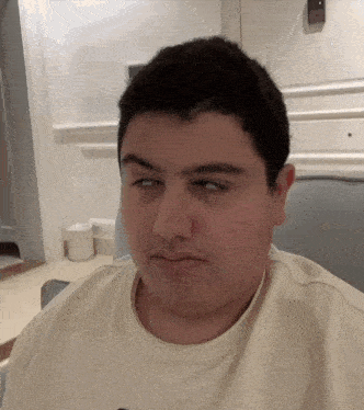 a man in a white shirt is sitting in a chair and making a funny face