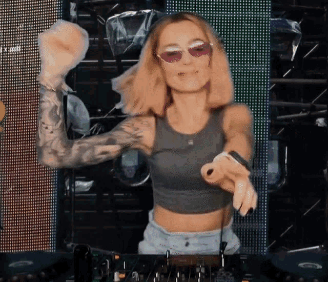 a woman wearing sunglasses and a gray tank top is dancing
