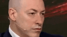 a bald man in a suit and tie is wearing a microphone on his head .