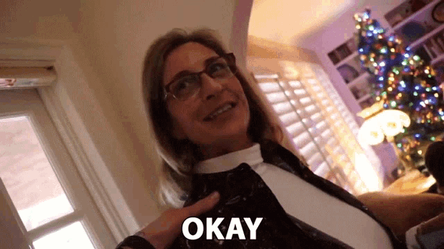 a woman wearing glasses is smiling and the word okay is above her