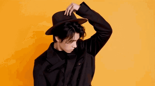 a man wearing a black hat and a black jacket is standing in front of an orange background .