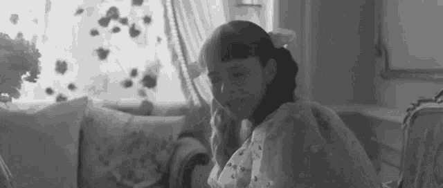 a black and white photo of a young girl sitting on a couch in a living room .
