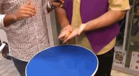 a group of people are standing around a blue table with their hands on it .