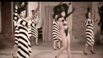 a group of women in striped dresses are dancing together on a stage .