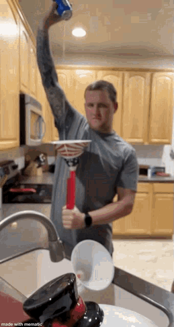 a man in a kitchen is holding a cup and a can of soda