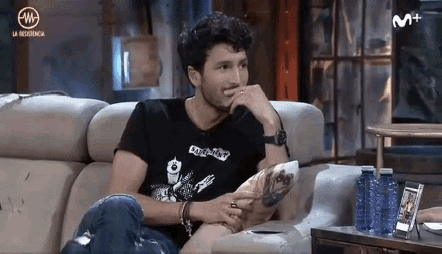 a man is sitting on a couch wearing a black shirt that says london
