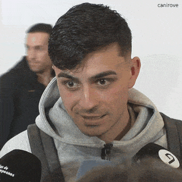 a man wearing a grey hoodie stands in front of two microphones with the letters canirove on them