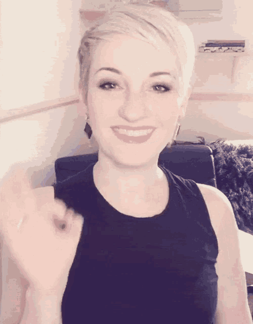 a woman with short blonde hair is smiling and waving her hand