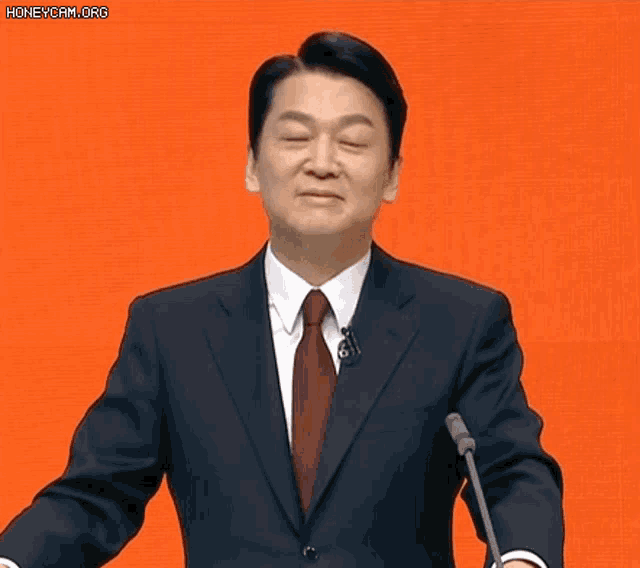 a man in a suit and tie is giving a speech in front of a microphone ..
