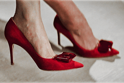 a woman wearing a pair of red high heels with a red bow