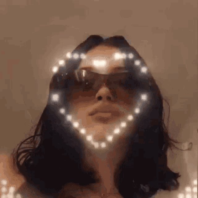 a woman wearing sunglasses and a necklace with a heart made of lights on her face .