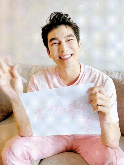 a man sitting on a couch holding a piece of paper with chinese writing on it and smiling