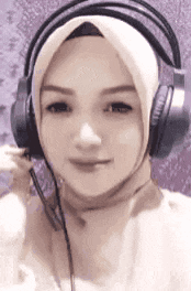 a woman wearing a hijab and headphones is smiling and looking at the camera .