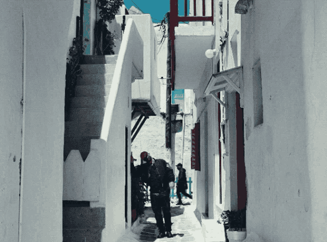 a man walking down a narrow alleyway with a sign that says ' athens ' on the side