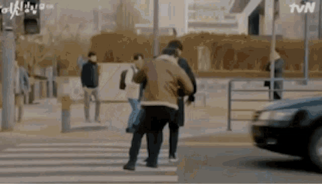 a group of people are crossing a street while a car is driving past .