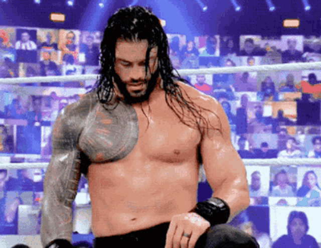 roman reigns is standing in a wrestling ring without a shirt .