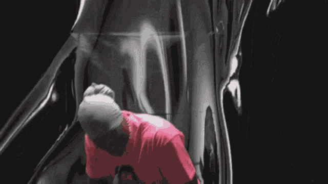 a man wearing a pink shirt and a white headband is sitting in a dark room