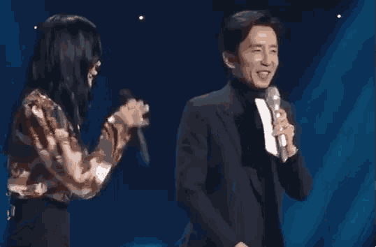 a man and a woman are standing next to each other on a stage . the man is holding a microphone .