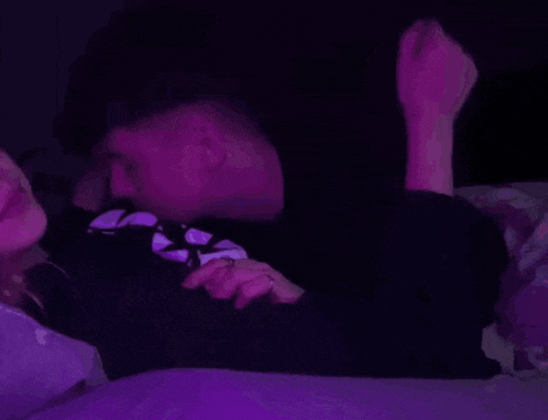 a man and a woman are laying on a bed in a dark room with purple lights .