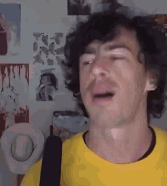 a man with curly hair is wearing a yellow t-shirt and a cowboy hat .