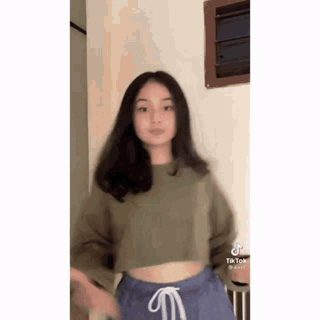 a young woman in a green crop top and blue shorts is dancing in a room .