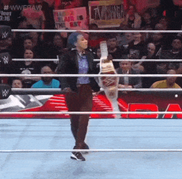 a woman in a suit is walking through a wrestling ring holding a championship belt .